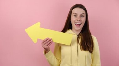 Sarı kağıt okla ortaya çıkan heyecanlı genç bir kadın kapüşonlu giyinmiş, reklam için fotokopi çekilen pembe renkli arka plan stüdyosuna izole edilmiş poz veriyor. İnsanlar duygusal yaşam tarzı konsepti