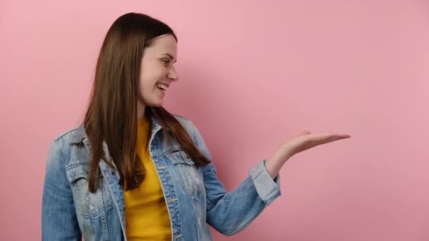 可爱的年轻女子把手指放在工作空间上 模仿被隔离在粉红工作室背景墙上的商业区 穿着牛仔夹克 人的情感生活方式概念 — 图库视频影像