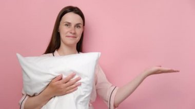 Pijamalı güzel, esmer bir kadın beyaz yastığı bir yana bırakıp, avuç içi açık bir şekilde fotokopi alanını gösteriyor. Gülümsüyor, mutlu, pembe renkli arka planda izole edilmiş poz veriyor.