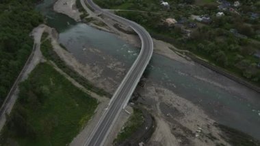 Vahşi nehir ve yeşil bitki örtüsünün üzerindeki yol köprüsünün üzerindeki güzel panoramik manzaranın havadan görüntüsü. İnsansız hava aracı bulutlu bir yaz gününde yol köprüsü boyunca uçar. Keşif ve seyahat hedefi
