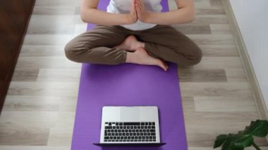 Genç sağlıklı esmer kadın spor kıyafetleri giyiyor. Meditasyon yapıyor. Namaste ellerini dizüstü bilgisayarda izliyor.