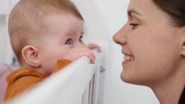 Sevgi dolu genç bir annenin yanında beyaz bir beşikte duran tatlı küçük kızının yan görüntüsü. Mutlu gülümseyen anne, uyuduktan sonra küçük kızla vakit geçiriyor. Annelik kavramı