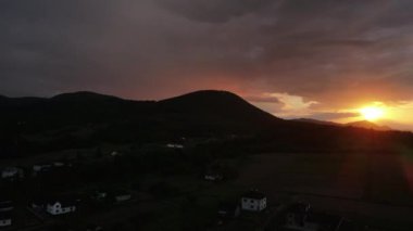 Yaz sabahında, turuncu günbatımında dağların insansız hava aracı görüntüsü. Güneş ışınları. Dağ sırasının yeşil orman yamaçları. Güneşin bulutlu gökyüzündeki parlak diski yavaşça dağların tepesine çıkar.