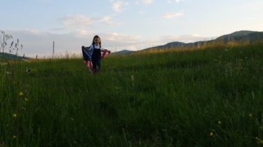 Güzel bir kızın koşuşunun, neşeli bir şekilde gülmesinin, rüzgarda Amerikan bayrağıyla oynaşmasının arka plandaki çocuğu kucaklamasının, özgür ve genç bir kadının el ele çekilmiş fotoğrafı. Yavaş çekim