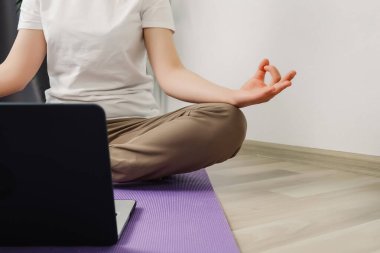 Lotus pozisyonunda meditasyon yapan tanınmamış bir kadın evde dizüstü bilgisayardan ders programını izliyor. Kadın oturma odasında sabah antrenmanı yapıyor. Nilüferli kadınların elleri yerde otururken poz verir.