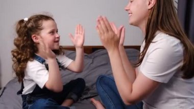 Sevimli küçük bir kız çocuğu eğlenceli bir anneyle pasta oynuyordu. Evde yatakta oturuyordu. Mutlu, genç bir aile annesi ve şirin küçük bir çocuk eğlenceli oyunlar öğreniyor. Birlikte güzel anların tadını çıkarıyorlar.