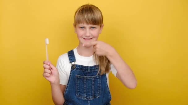 可爱可爱可爱的金发女学生的特写 手握着 指指着牙刷 像一个手势 在黄色的背景墙上显得孤立无援 口腔卫生概念 — 图库视频影像