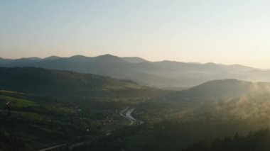 Güneş doğarken kırsal bölgelerin insansız hava aracı görüntüleri. Doğa ilhamı. Kırsal alanda küçük binalar, nehir, arka plan dağları manzaralı yol. Turizm ve seyahat tutkusu konsepti