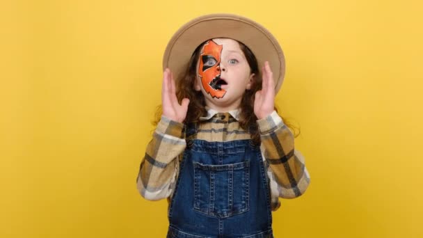 할로윈 마스크를 충격적 소녀의 카메라를 두려워 모자와 셔츠를 스튜디오의 노란색 — 비디오