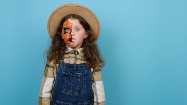 ハロウィーンの化粧マスクを持つ動機の小さな女の子の子供は 帽子とシャークを身に着けており 衝撃的な子供のポイントを離れて 青のスタジオの背景に隔離されたポーズで方向を示しています パーティーの休日のコンセプト — ストック動画