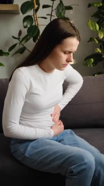 Karın ağrısı çeken, karın ağrısı çeken hasta bir kadın mide iltihabı belirtileri gösteriyor. Üzgün kadın koltukta oturup hazımsızlık çeken mide gazı sorunu yaşıyor.