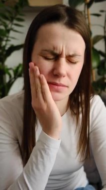 Yanağına dokunan genç bir kadın, dişleri ağrıyan bir kadın. Mutsuz olmak kötü hissettiriyor. Ağızda hastalık, sinir ağrısı ve azı dişi. Diş ağrısı ve diş sağlığı, çene ağrısı, sağlık konsepti