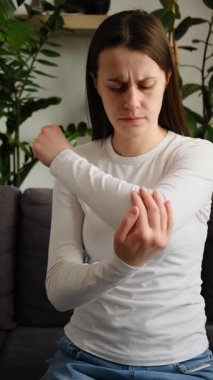 Dirsek ağrısı olan, sağlıksız, üzgün, beyaz bir kadın evde koltukta tek başına masaj yapıyor. Sağlık, eklem iltihabı dirsek kavramında ağrı