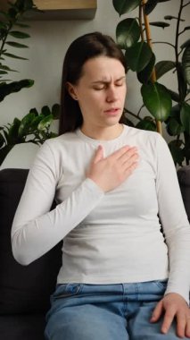 Kanepede tek başına otururken göğüs ağrısı çeken, sağlıksız, genç, beyaz bir kadın evde kalp ağrısı, enfarktüs ya da kalp hastalığı konsepti olan üzgün bir kadın.