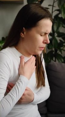 Kanepede yalnız başına otururken göğsü ağrıyan sağlıksız, üzgün genç bir kadın evde kalp ağrısı çekiyor. Grip mevsiminin kış konseptindeki belirtileri