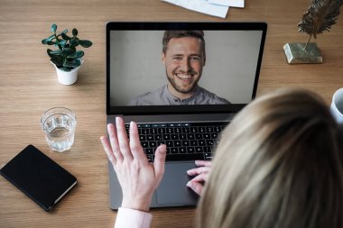 Bilgisayarında çalışan uzaktan kumandalı bir çalışan kadın bir toplantıda video konferansı ya da web sunumu izlemek için konuşurken, flört ederken ve el sallarken bilgisayarının başında.