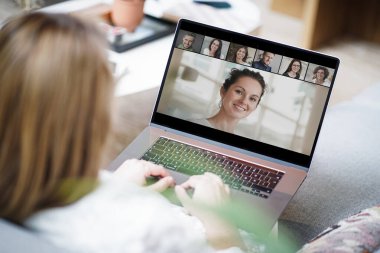 Uzaktan kumandalı, çalışan sarışın bir kadın evinde dizüstü bilgisayarla kanepede oturmuş bir online takım toplantısına katılıyor ve video konferansı ya da web sunumu izliyor.