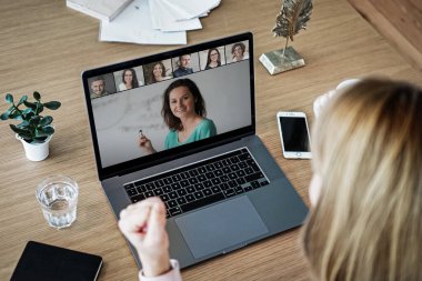 Uzaktan kumandalı online çalışan bir kadın iş masasında laptopuyla oturuyor ve bir online toplantıya katılıyor ya da video konferansı veya webinar sunumu izliyor.