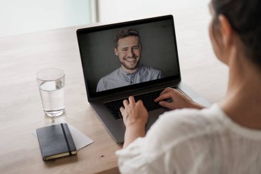 Uzaktan kumandalı online çalışan bir kadın iş masasında laptopuyla oturuyor ve bir online toplantıya katılıyor ya da video konferansı veya webinar sunumu izliyor.