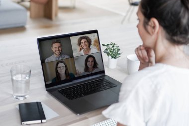 Uzaktan kumandalı online çalışan bir kadın iş masasında laptopuyla oturuyor ve bir online toplantıya katılıyor ya da video konferansı veya webinar sunumu izliyor.