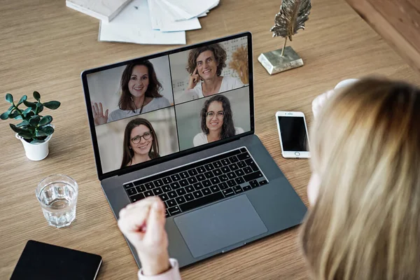 Uzaktan kumandalı online çalışan bir kadın iş masasında laptopuyla oturuyor ve bir online toplantıya katılıyor ya da video konferansı veya webinar sunumu izliyor.