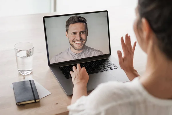 remote online working woman on her laptop in home office on a desk while talking, flirting and waving hand in a video chat to greet team in a meeting - watching video conference or webinar presentation