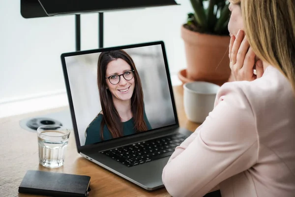 Uzaktan kumandalı online çalışan bir kadın iş masasında laptopuyla oturuyor ve bir online toplantıya katılıyor ya da video konferansı veya webinar sunumu izliyor.