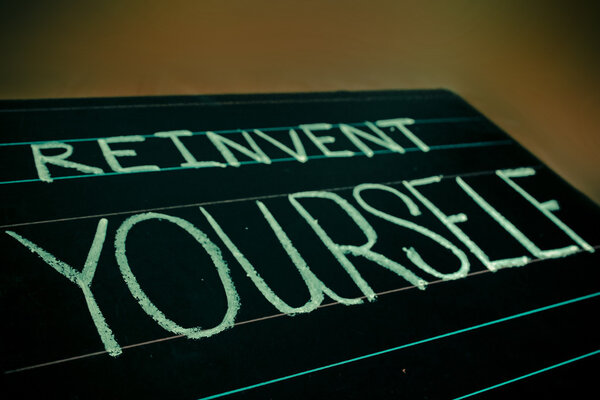 reinvent yourself phrase handwritten on black chalkboard