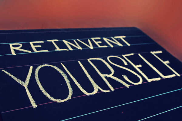 reinvent yourself phrase handwritten on black chalkboard