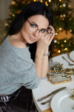 Mavi gözlü ve gözlüklü manken kız Noel kahvaltısı için bir masada oturuyor.