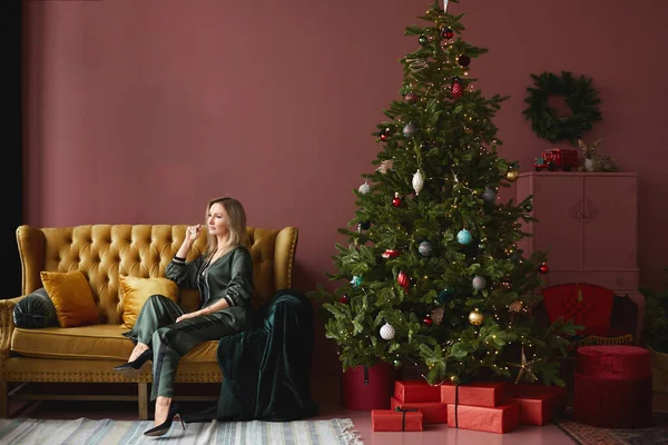 Modelo chica en ropa de moda se sienta en el sofá amarillo cerca del árbol de Navidad en el interior vintage — Foto de Stock