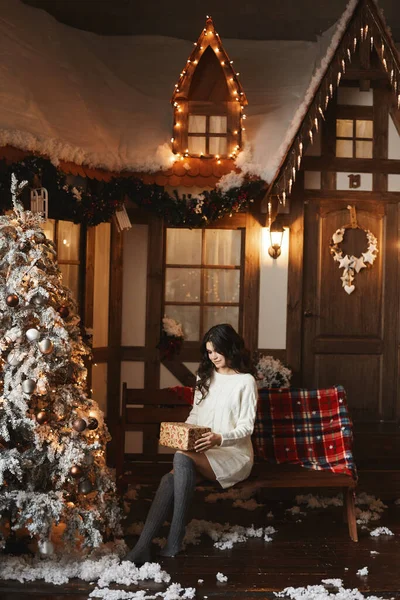 Jeune femme en tricot robe et bas garde un cadeau de Noël et posant dans un intérieur décoré — Photo