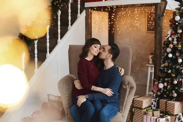 Jeune homme beau câlin une fille brune dans le fauteuil dans un salon près du sapin de Noël — Photo