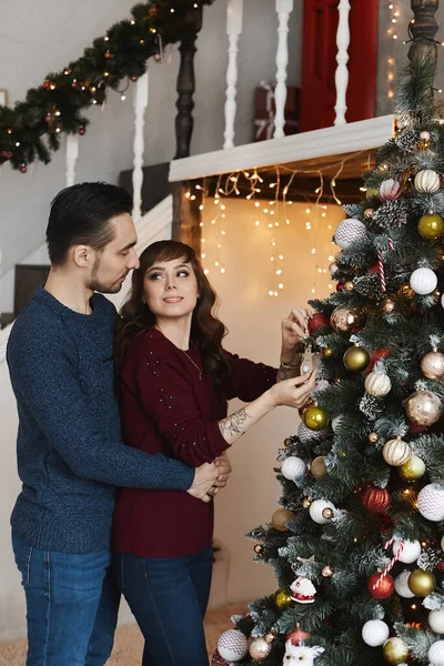 Un jeune homme et une jeune femme décorant ensemble le sapin de Noël dans le salon intérieur pour les vacances de Noël — Photo