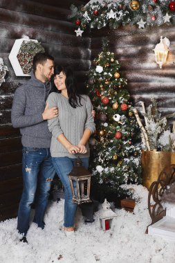 Güzel bir çift, şık yakışıklı bir adam ve modaya uygun gri tişörtlü genç bir esmer, Noel için iç mekânda sarılıp poz veriyorlar.