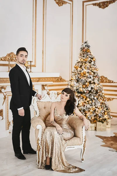 Beau homme en costume noir et un jeune modèle dans une robe de soirée à la mode posant dans l'intérieur de luxe décoré pour le temps de Noël — Photo
