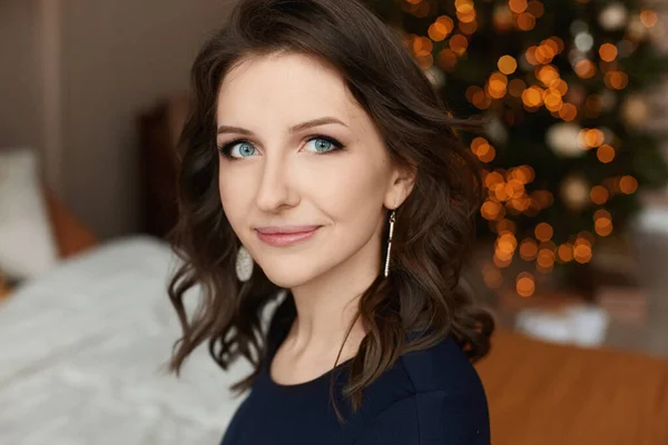 一个年轻女子的画像，蓝眼睛，柔和的妆容，背景上挂着节日的圣诞彩灯 — 图库照片