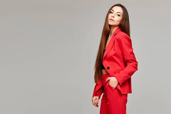 Sidovy av modellen flicka med långt hår i snygg röd kostym isolerad vid den grå bakgrunden med kopieringsutrymme — Stockfoto