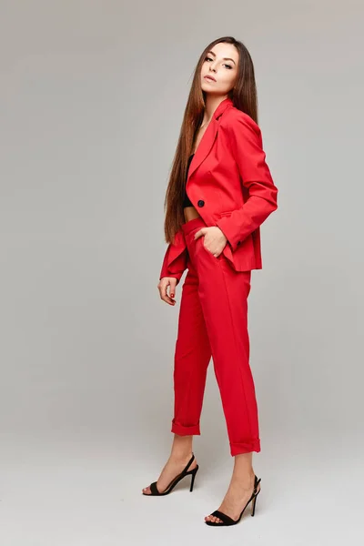 Full längd porträtt av modellen flicka med långt hår i snygg röd kostym isolerad vid den grå bakgrunden med kopia utrymme — Stockfoto
