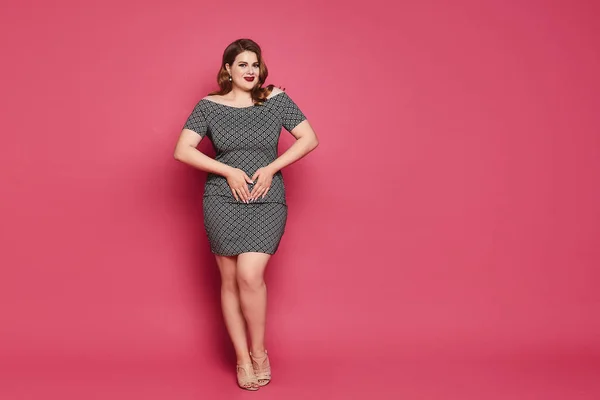 Модель plus-size с ярким макияжем и стильной прической в коротком платье, изолированном на розовом фоне — стоковое фото