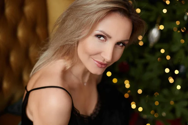 Πορτρέτο μιας πανέμορφης γυναίκας με ξανθά μαλλιά και τέλειο μακιγιάζ με εορταστικά χριστουγεννιάτικα φώτα στο παρασκήνιο — Φωτογραφία Αρχείου