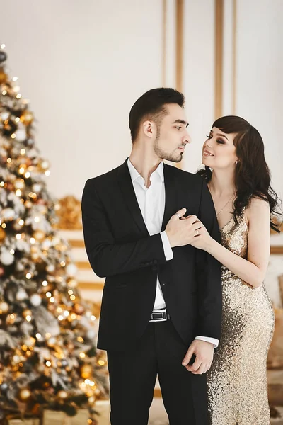 Modèle fille dans une élégante robe en or et beau monsieur dans un costume noir posant dans un intérieur de luxe près de l'arbre de Noël — Photo