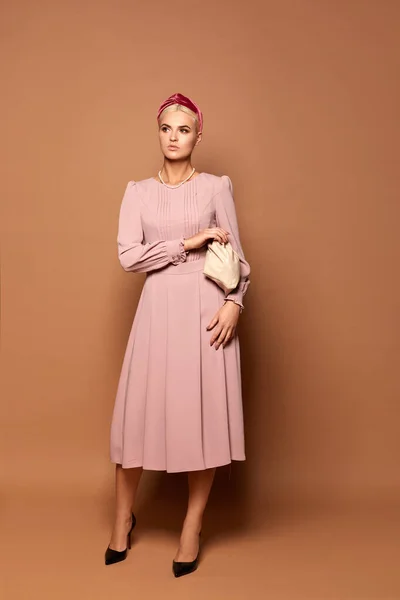 Bonita modelo dama lleva un lindo vestido rosa con mangas largas aisladas en el fondo beige. Foto de moda con espacio de copia para su anuncio o logotipo — Foto de Stock