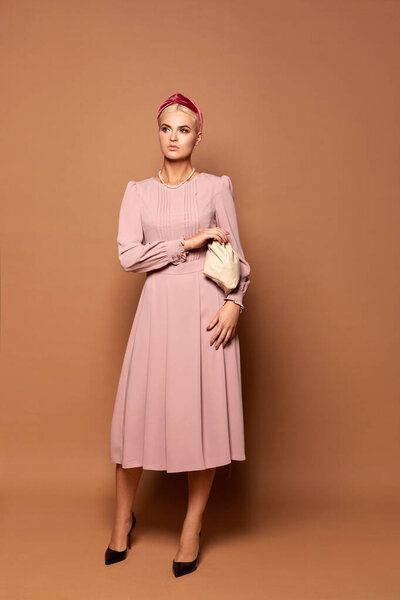 Pretty model lady wears a cute pink dress with long sleeves isolated at the beige background. Fashion photo with copy space for your advertisement or logo