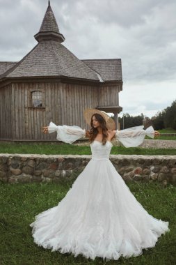 Kırsalda bir düğün gününde uzun kollu, klasik bir elbise içinde güzel bir gelin. Eski moda gelinlik ve açık havada poz veren hasır şapkalı genç bir kadın. Düğün modası kavramı