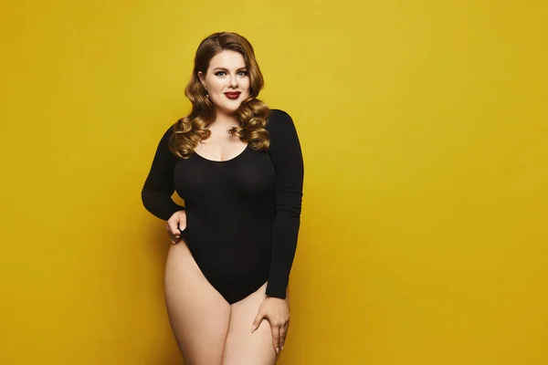 Linda mulher modelo plus-size com maquiagem brilhante em bodysuit preto posando sobre fundo amarelo, isolado. Jovem mulher gorda sexy — Fotografia de Stock