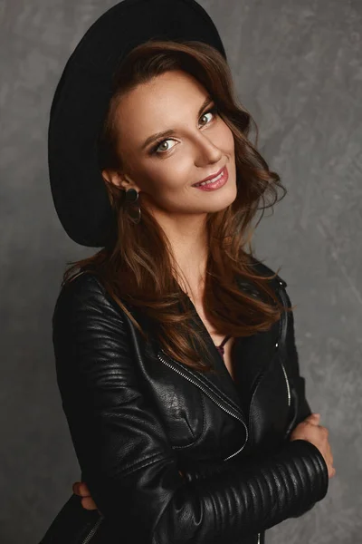 Retrato de jovem modelo mulher com maquiagem brilhante e pele perfeita em um chapéu preto na moda e jaqueta de couro — Fotografia de Stock