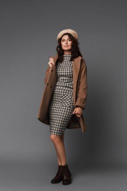 Gri arka planda izole edilmiş şık bahar kıyafetli zarif bir kadın. Gri arka planda poz veren bereli şapkalı ve bej ceketli model kadın.