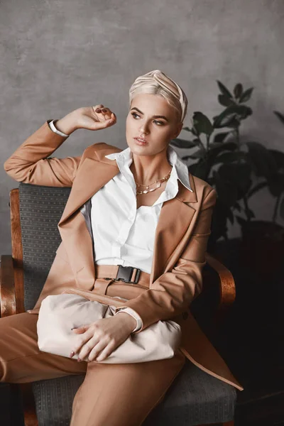 Porträtt av högmodern kvinna med perfekt makeup i trendig beige kostym. Modell flicka i fashionerade kläder poserar i en vintage fåtölj — Stockfoto