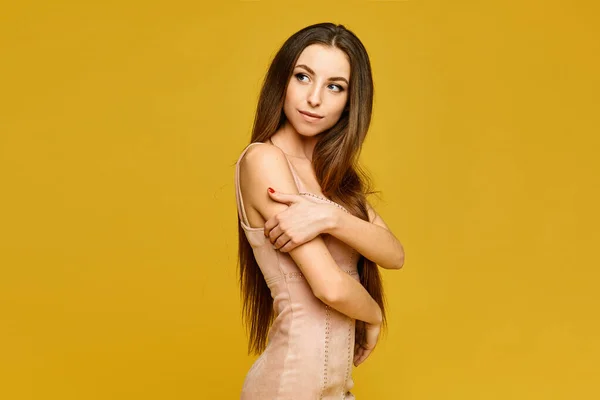 Retrato de la joven modelo mujer con el cuerpo delgado y el pelo largo que lleva en un vestido beige aislado en el fondo amarillo con espacio de copia — Foto de Stock